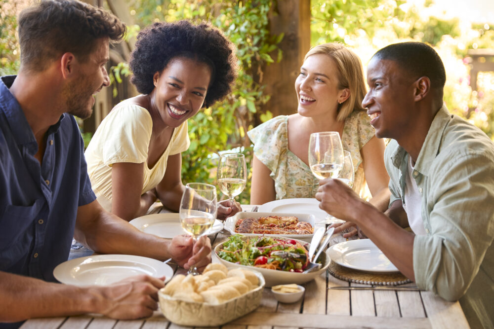 Group Of Smiling Friends Outdoors At Home Eating Meal And Drinking Wine Together